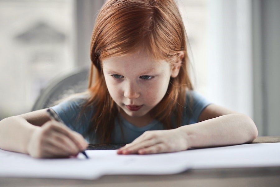 Young girl sits at table writing on paper.
