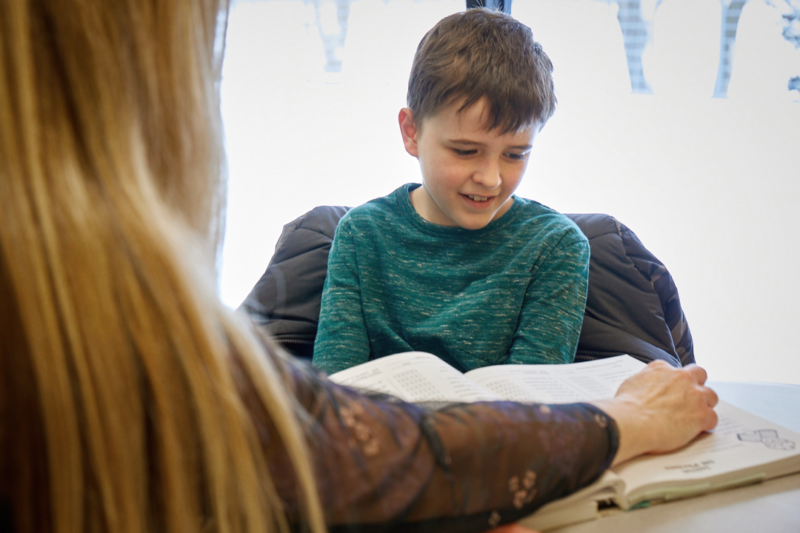 young boy sits at table reading